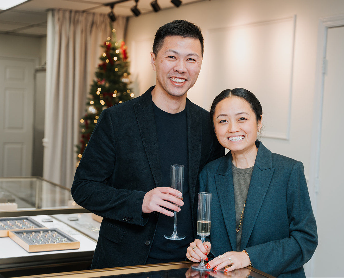 Two people holding champagne glasses in a festive indoor setting with a Christmas tree.